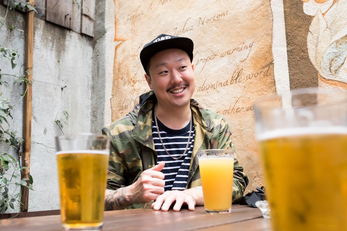 A man wearing a hat sits at a table with a pint of beer.