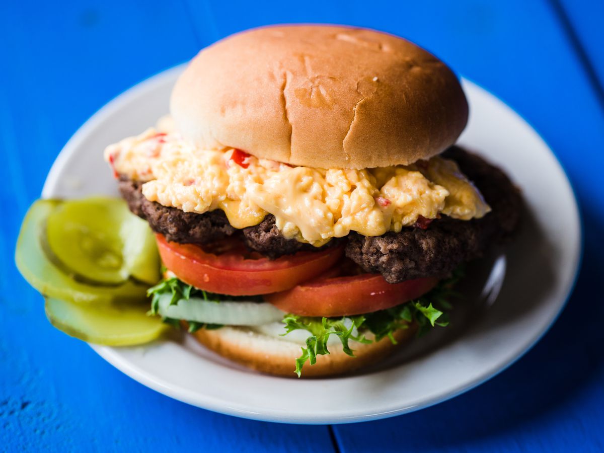 A burger topped with pimento cheese on a blue table. 