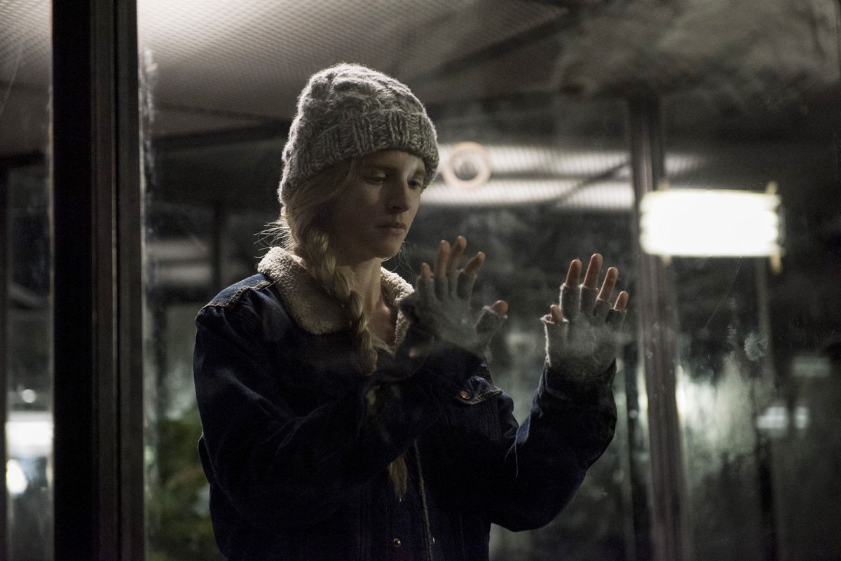 Prairie Johnson in a coat, knit cap, and fingerless gloves pressing her hands against a smudged glass pane in The OA.