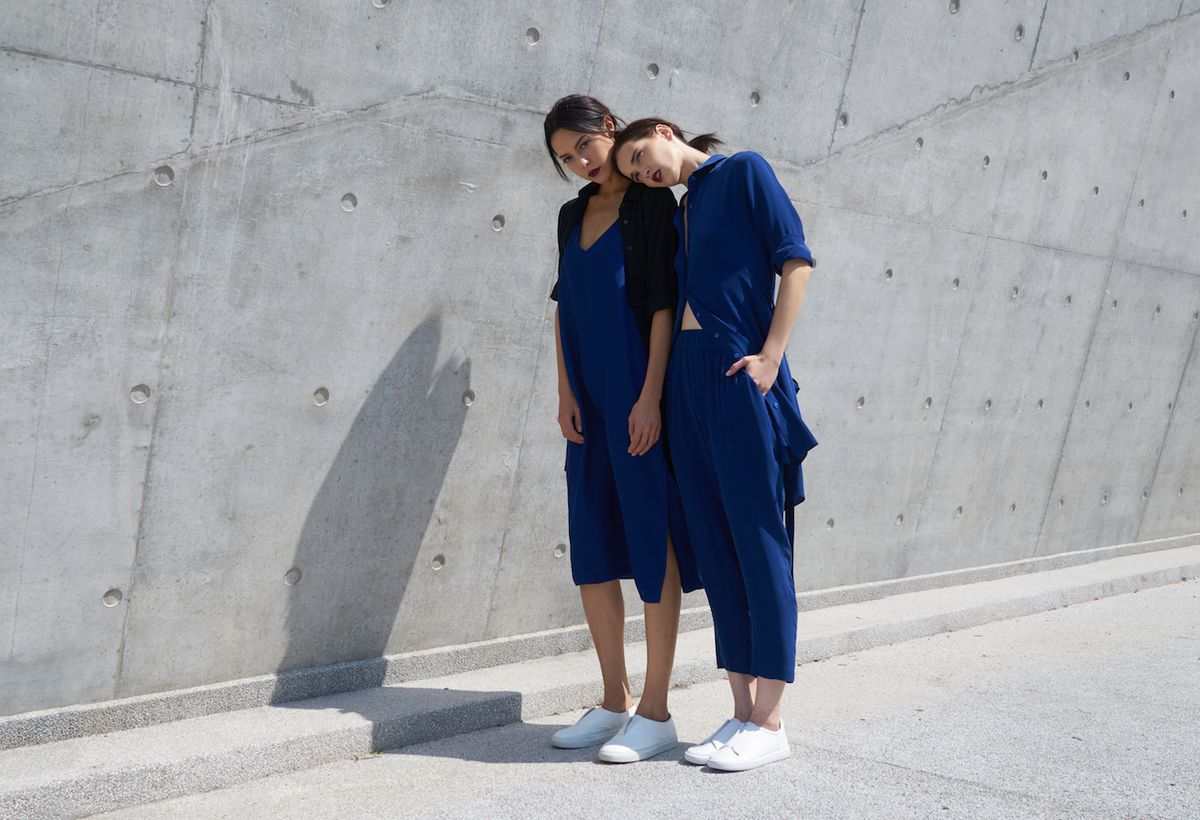 Two women in blue jumpsuits wearing white sneakers standing in front of a gray wall