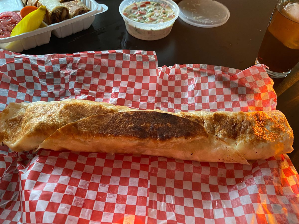 A very long, griddle shawarma wrap, show on the red-and-white checkered paper that it had been wrapped in