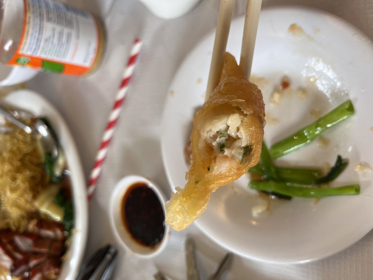 A prawn dumpling suspended over a table by chopsticks, one bite taken.