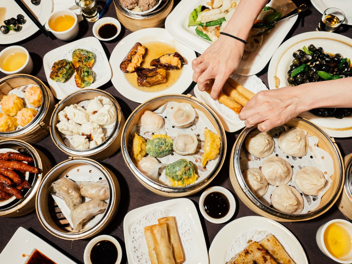 A table is crowded with various dim sum, including chicken feet, stuffed eggplant, and spring rolls.