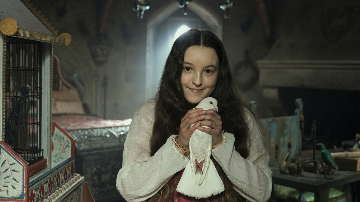 a young teenage girl with long brown hair and pale skin clutches a white dove; she wears medieval style clothes