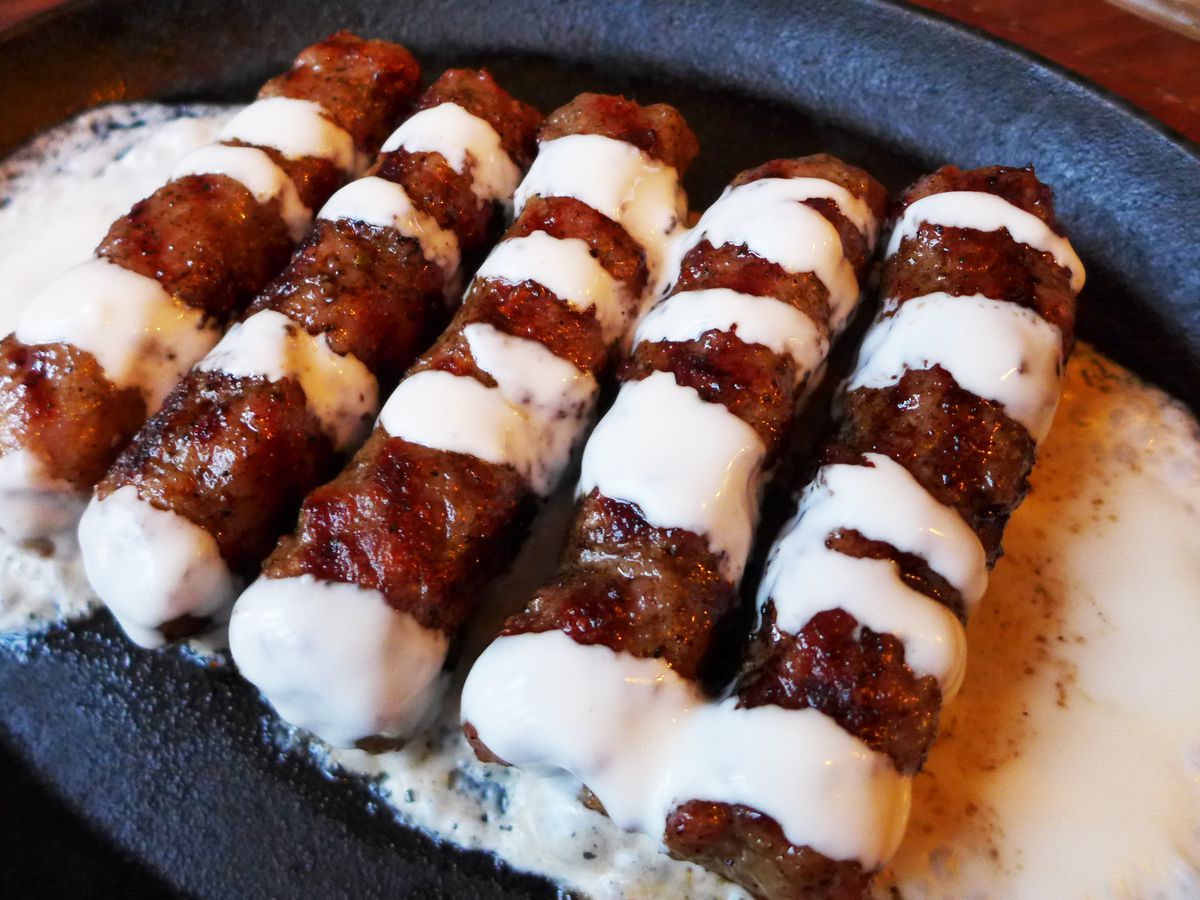 A line of brown skinless sausages striped with cream sauce.