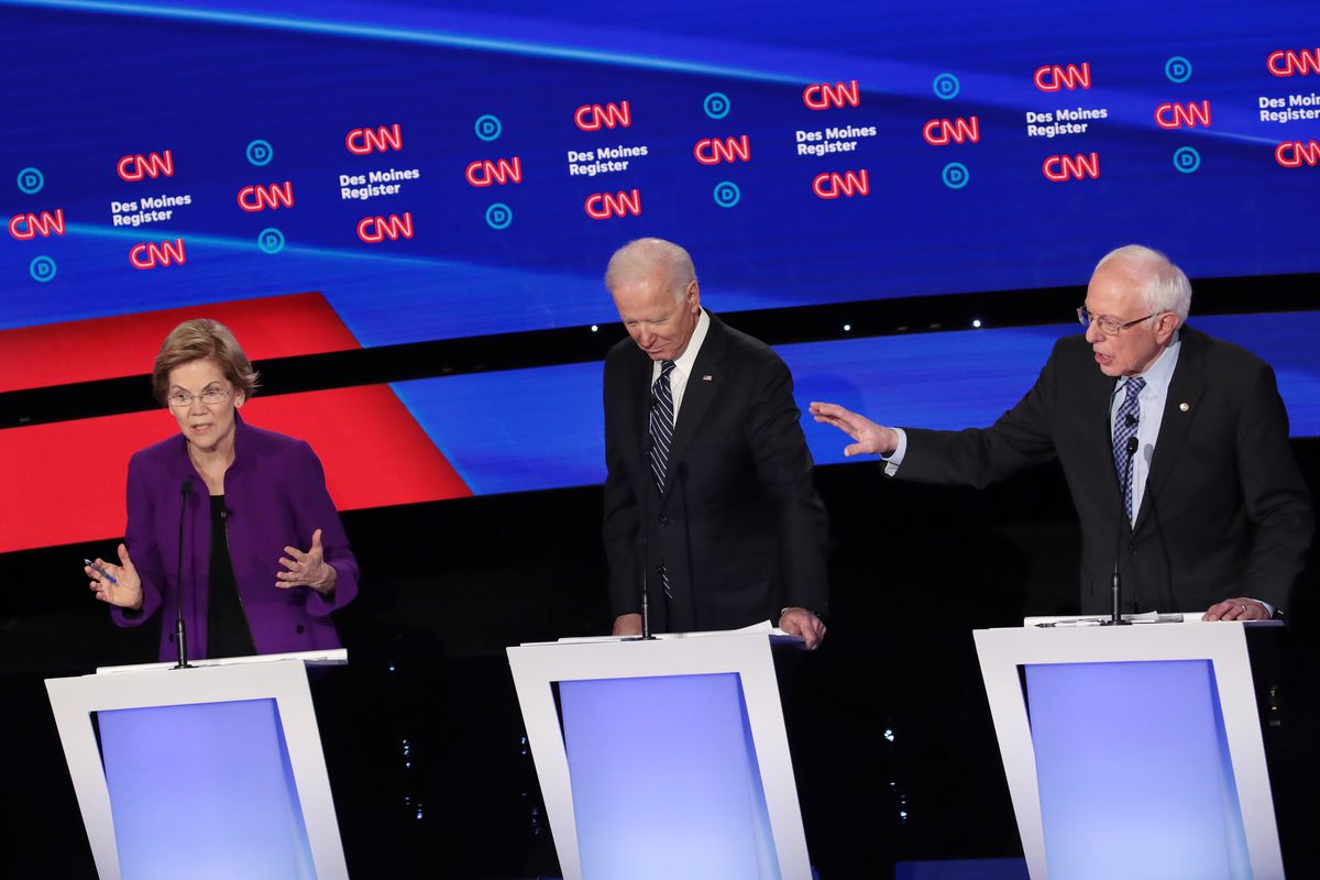 Senator Elizabeth Warren and Senator Bernie Sanders speak on the debate stage as Joe Biden  listens.