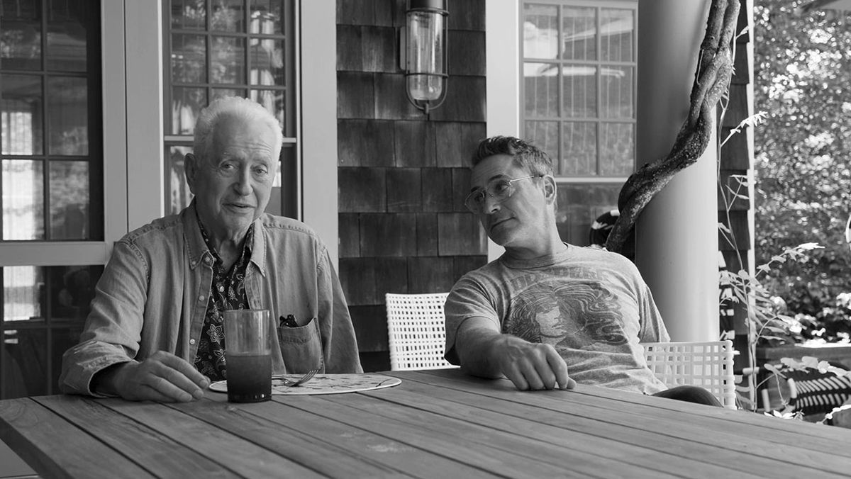 Robert Downey Jr. looks lovingly at his father as they sit at a table in a black-and-white image.
