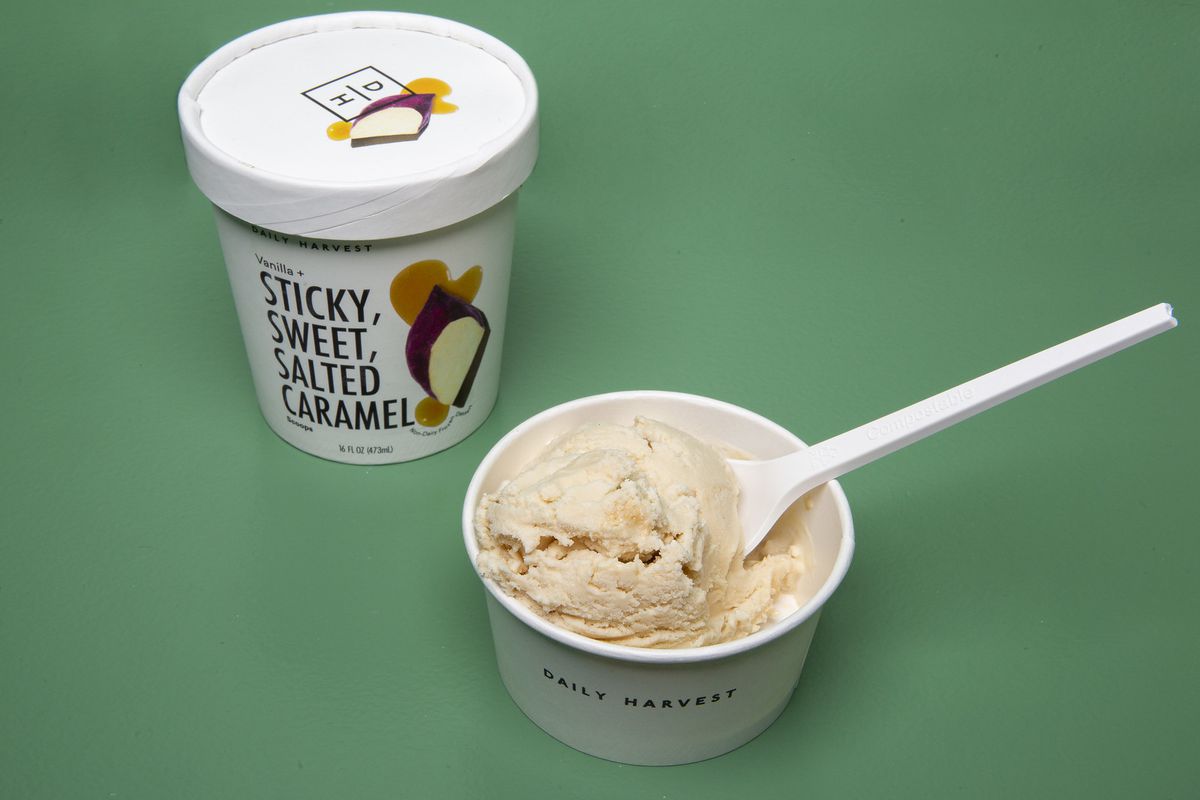 A carton of ice cream and a small cup with a scoop of ice cream and a plastic spoon