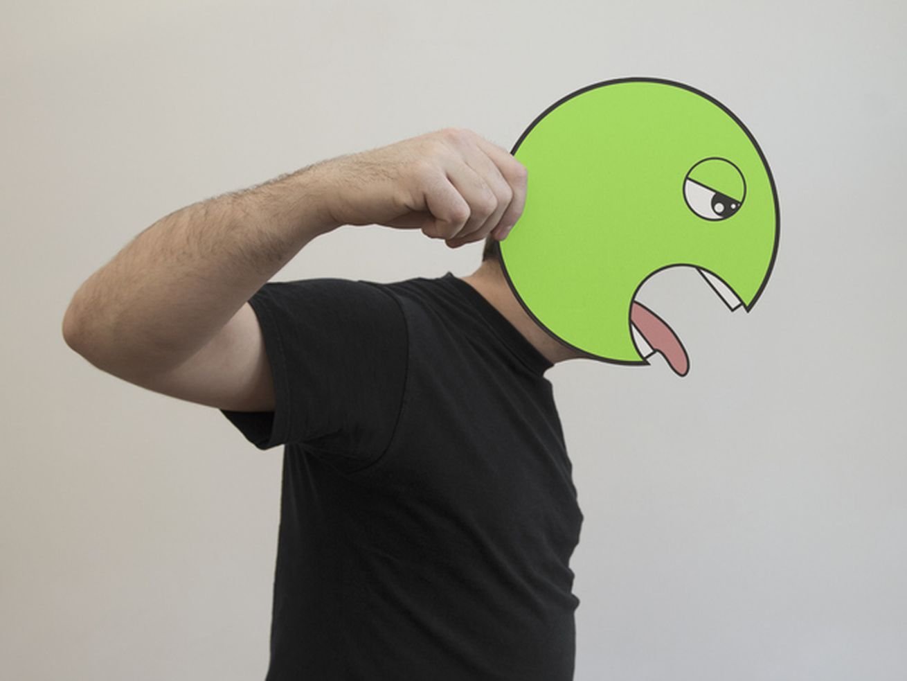 A photo of a man holding a vomiting emoji over his face in profile.
