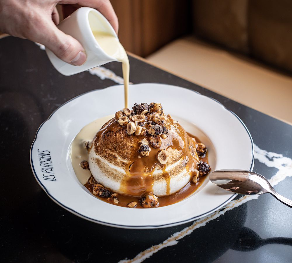 A server pours cream over a layered merengue topped with chopped hazelnuts.