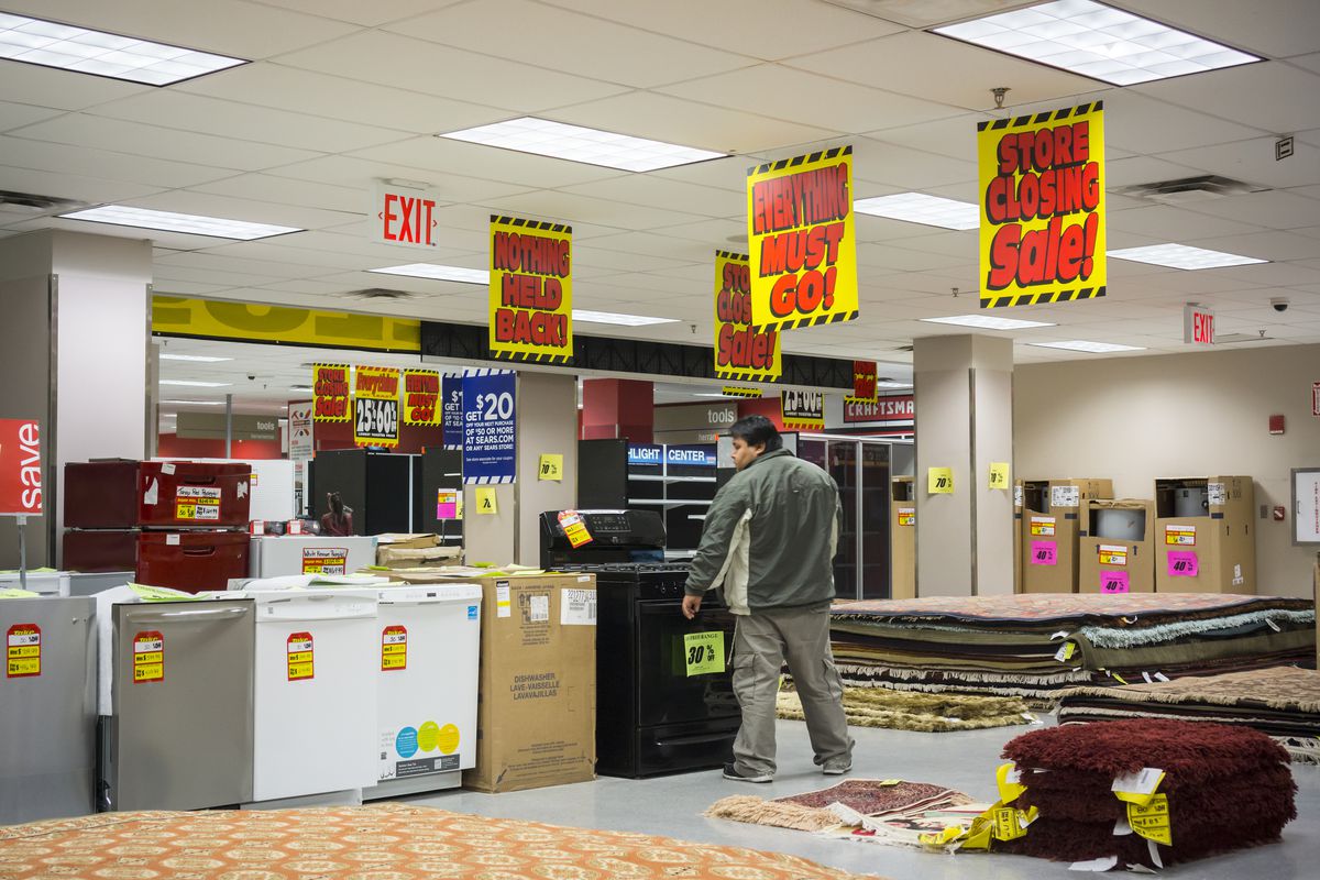 A man stands below “Everything must go!” signs.