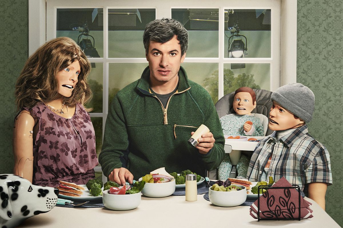 Key art from Nathan Fielder’s show The Rehearsal shows him seated at a meal surrounded by mannequins of family members.
