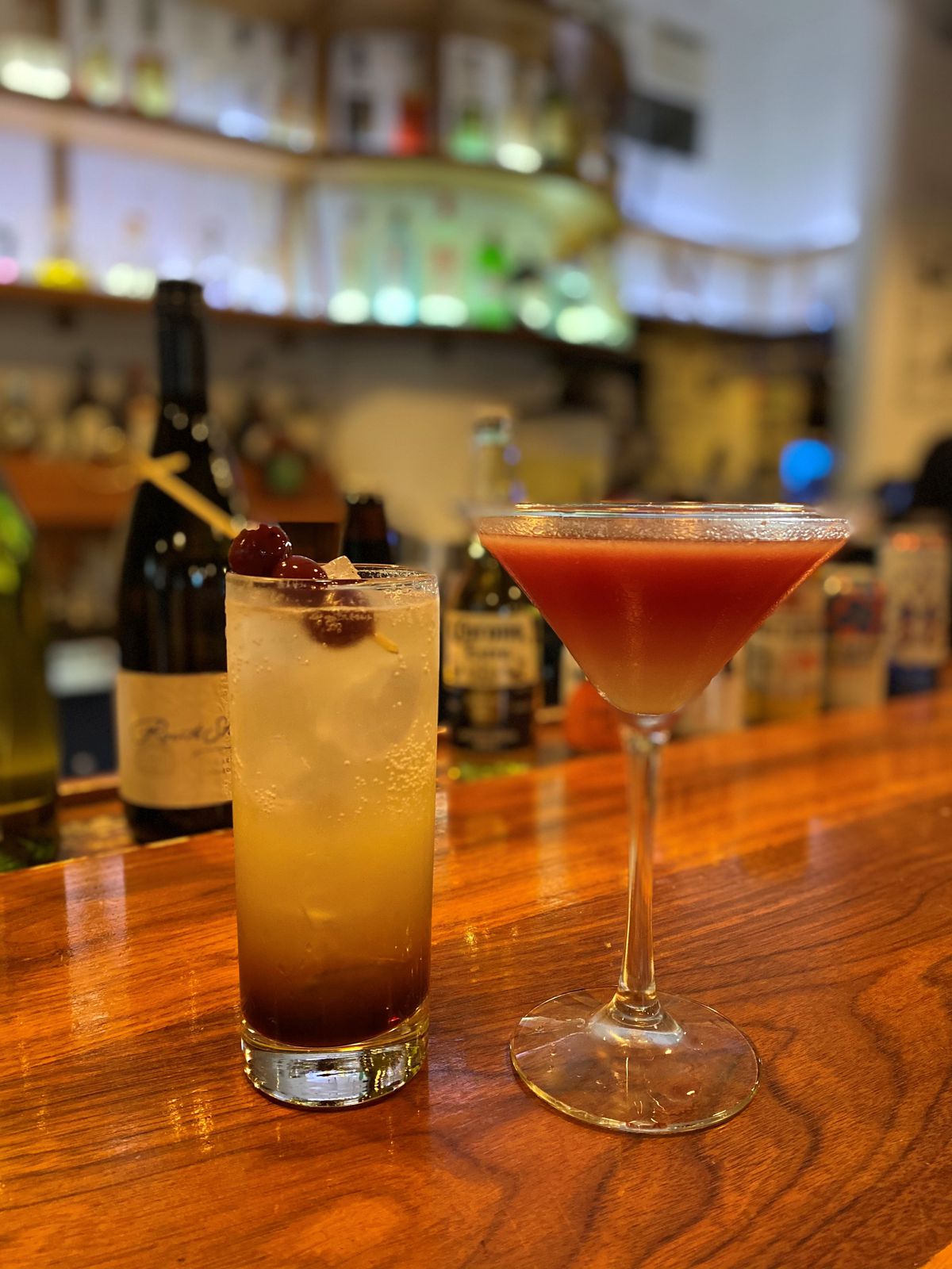 Two cocktails sitting side by side on a wooden bar counter