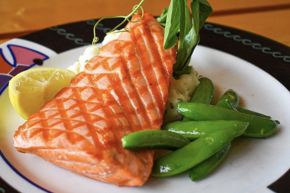 Chargrilled salmon on a white plate with a side of pea pods and a slice of lemon