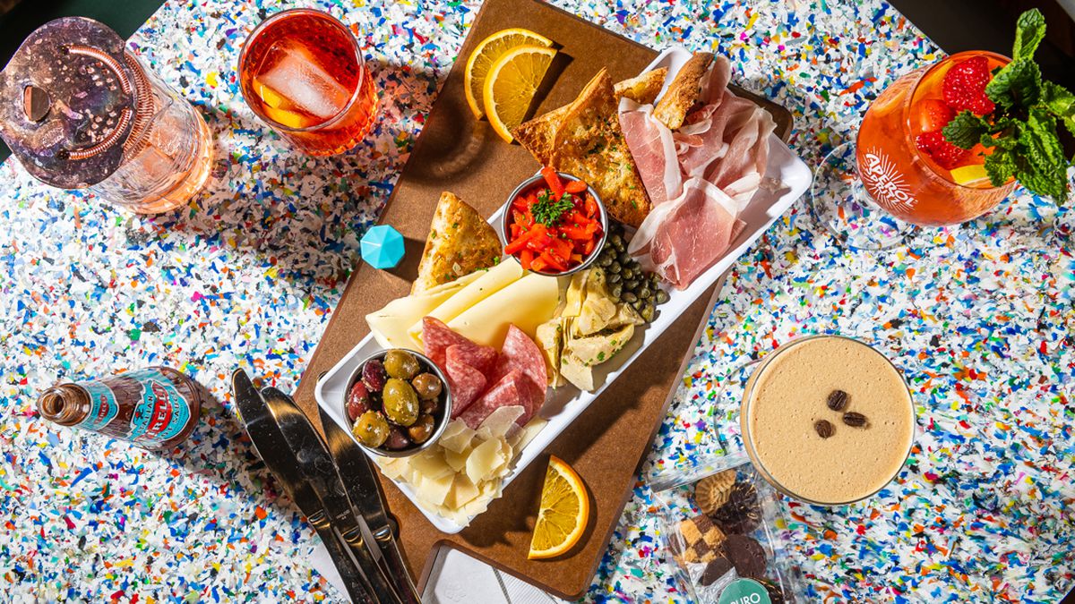a color-specked table topped with a meat and cheese tray and cocktails