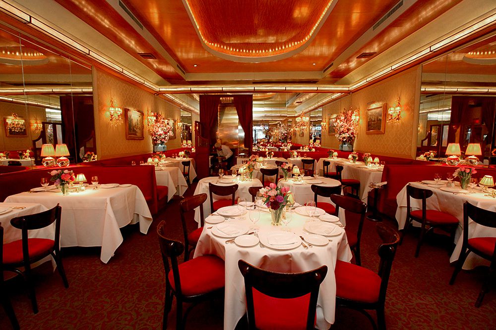 A sprawling, ornate dining room with red chairs, mirrored walls, and fine tableware.