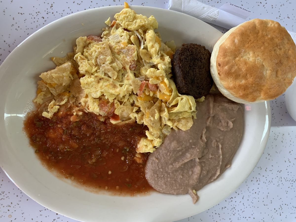 A plate of eggs, red salsa, creamy beans, a sausage patty, and biscuit.