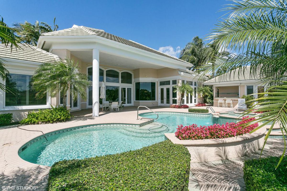 A Florida home with a large column in between the pool and the outdoor living area with a barbecue nearby.