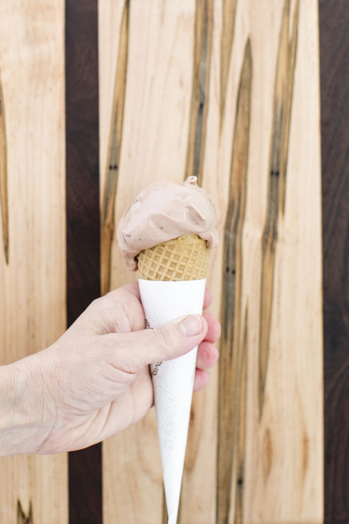 A hand holding a sugar cone of malted milk ball gelato