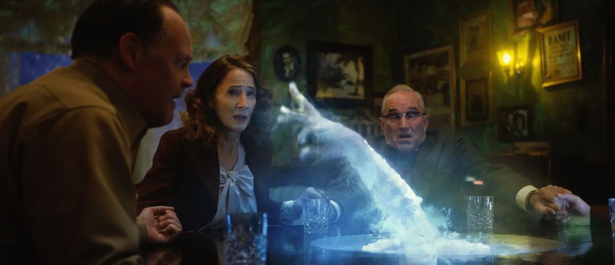 (L-R) Jeremy Holm, Anne Ramsay, and Ron E. Rains holding hands around a table as a ghostly hand reaches out at them in Brooklyn 45.