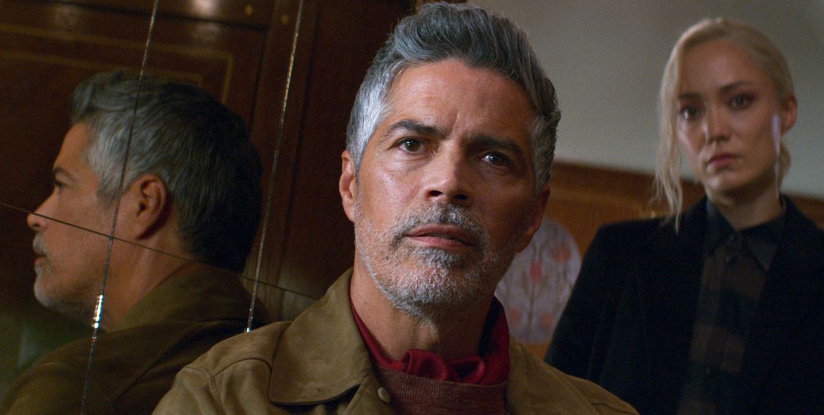 Gabriel (Esai Morales), a man grey hair and a grey-and-white goatee, stands in a wood-paneled train cabin and stares into the camera as his lackey Paris (Pom Klementieff) looms threateningly in the background in Mission: Impossible – Dead Reckoning Part One