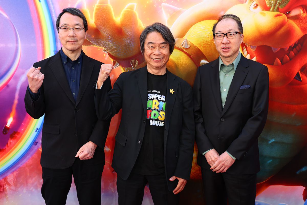 Takumi Kawagoe, Shigeru Miyamoto and Koji Kondo attend a screening The Super Mario Bros. Movie. The three pose on the red carpet, left to right, in front of a movie poster.