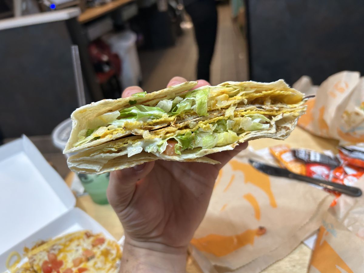 A hand clutches a Crunchwrap Supreme from Taco Bell under artificial lighting.