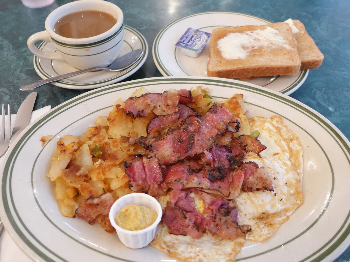 A breakfast plate with toast, coffee, and fried eggs, with pastrami that looks like bacon.