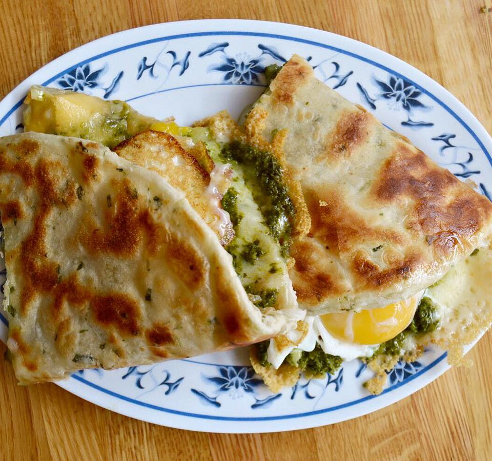 scallion pancake “sandwich” stuffed with greens and oozy eggs on a white plate with a blue floral border