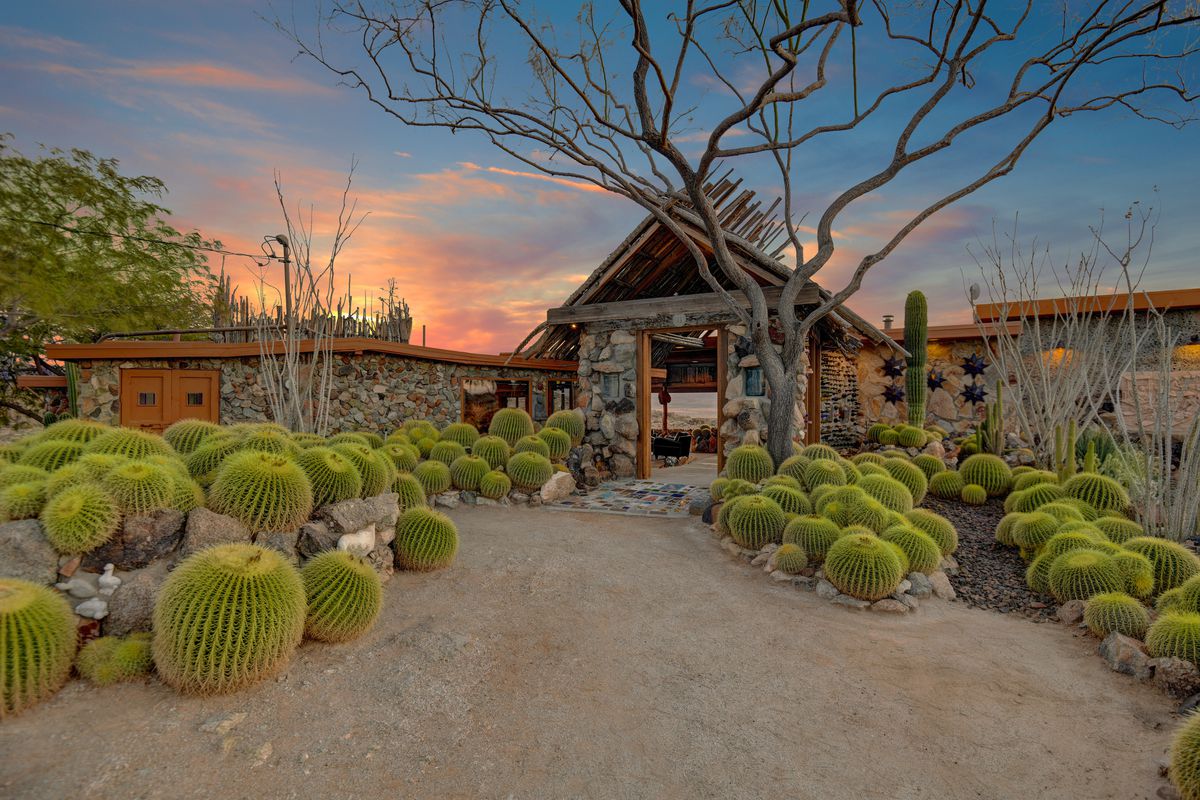 A wood and stone house sits in a landscaped desert garden with cacti and paths. 