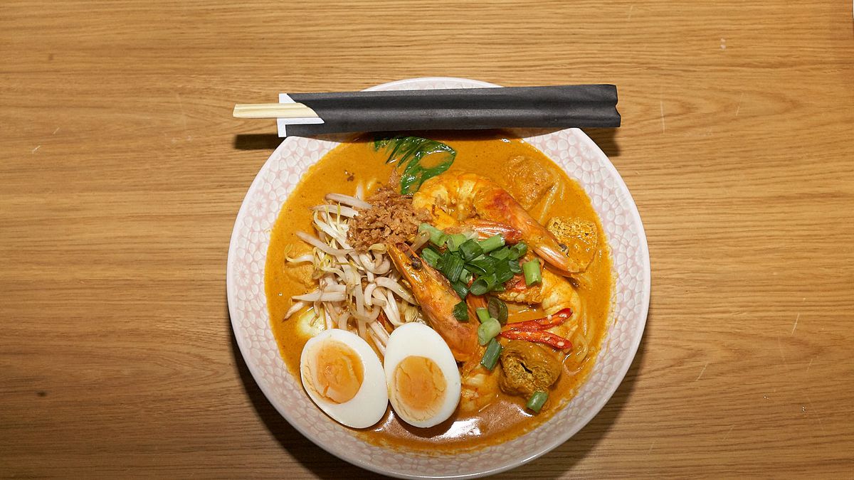 A large bowl of curry laksa with eggs and vegetables peaking out of the broth, and chopsticks resting on the rim.