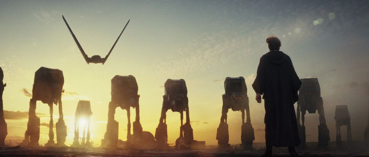 A plane soars behind a group of AT-ATs on a sunlit planet, as Luke Skywalker stands in front of them in The Last Jedi.