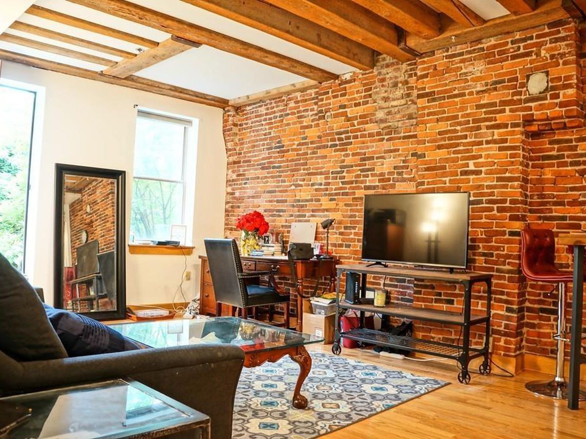 A living room with a high ceiling, beams on that ceiling, and a large exposed brick wall.