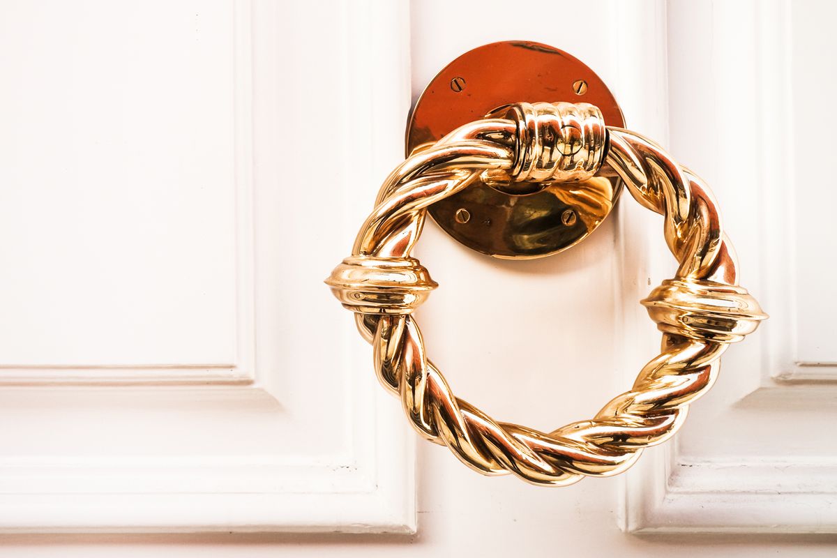 Gold circular door knocker on a white door.
