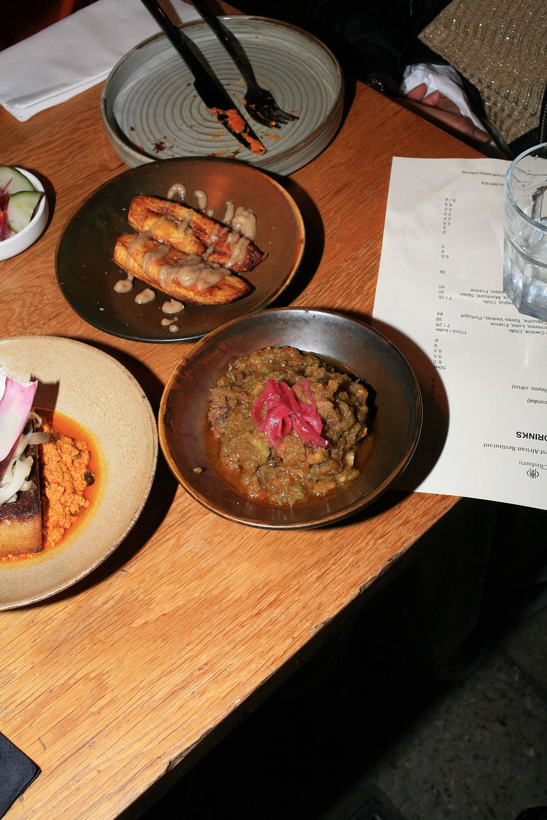 In the foreground: Goat ayamase, a stew with green peppers, garnished with pickled red onions. Plantain behind. 