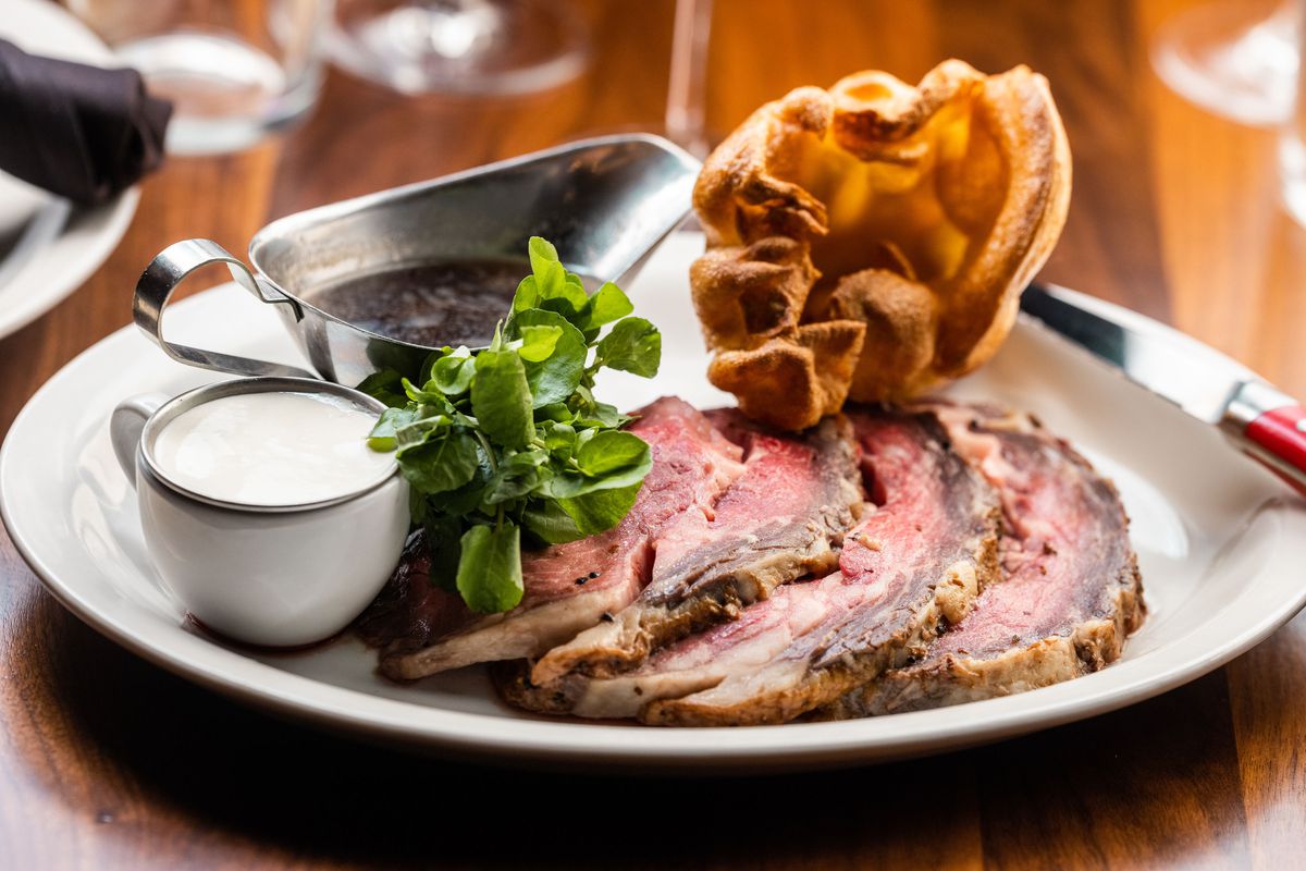 A steak sits on a plate with a Yorkshire pudding plus steak sauces.