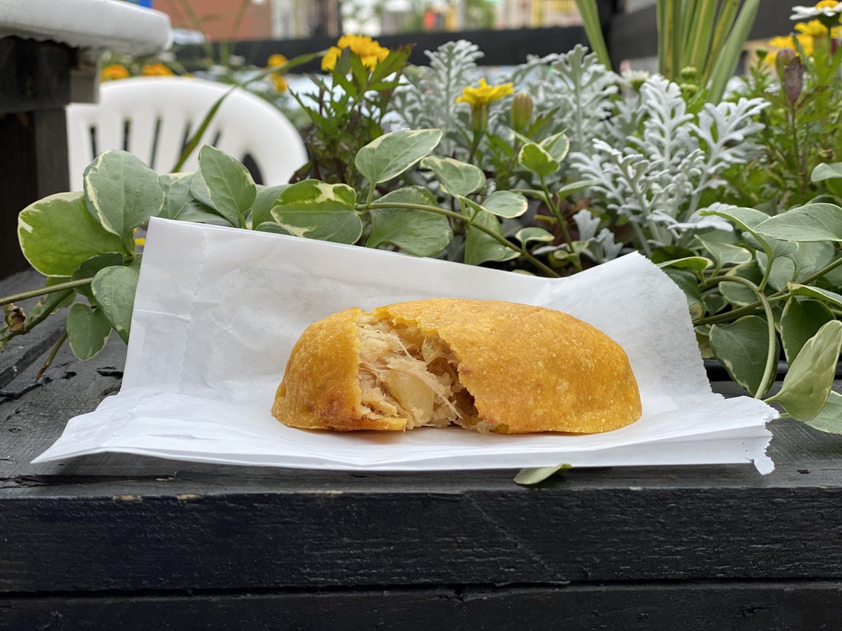 A yellow corn empanada sits on wax paper in an outdoor garden