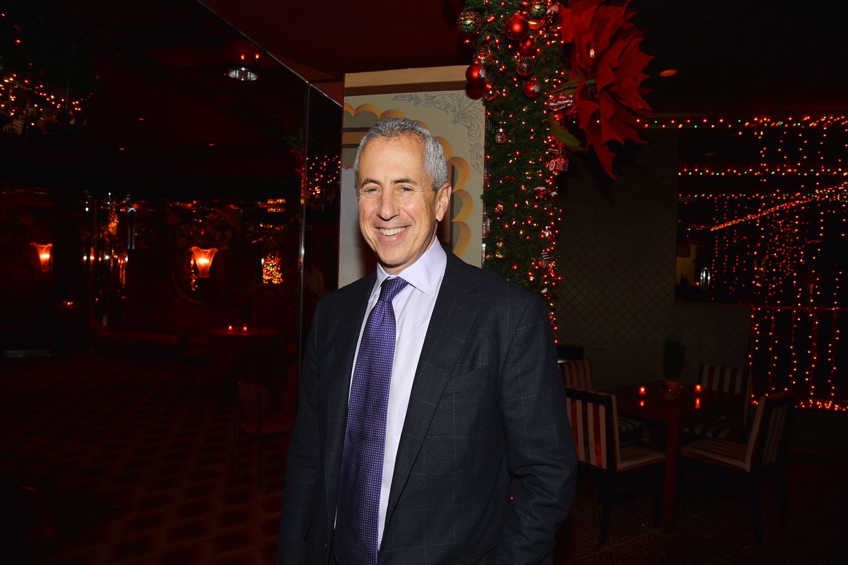 A man stands and smiles at the camera in a suit and dark tie at a holiday party in NYC in 2018.