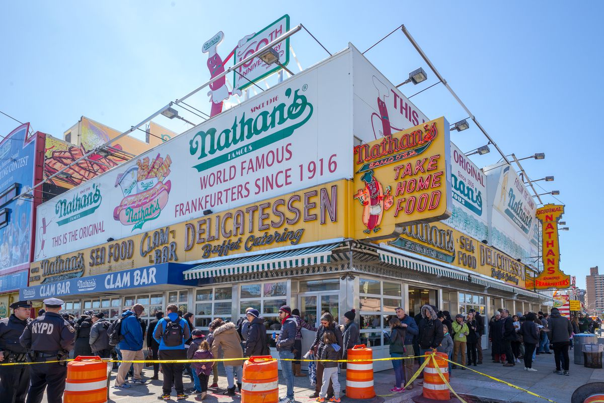 Customers wait in a line that wraps around the corner of the colorful Nathan’s Famous restaurant in Coney Island.