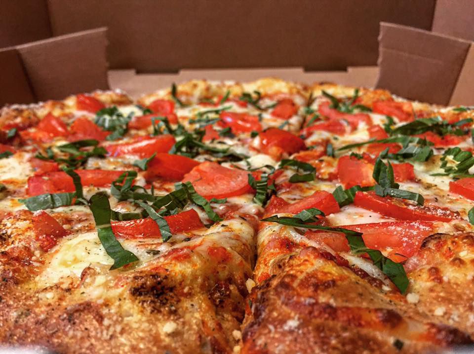 Pizza with tomato and basil in a takeout box