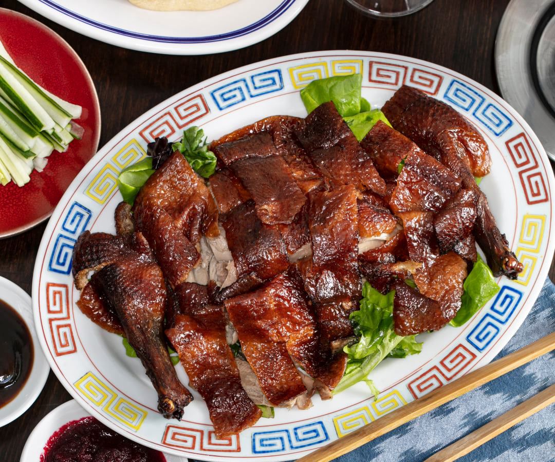 a whole, sliced Peking duck on a plate surrounded by other plates of Chinese food