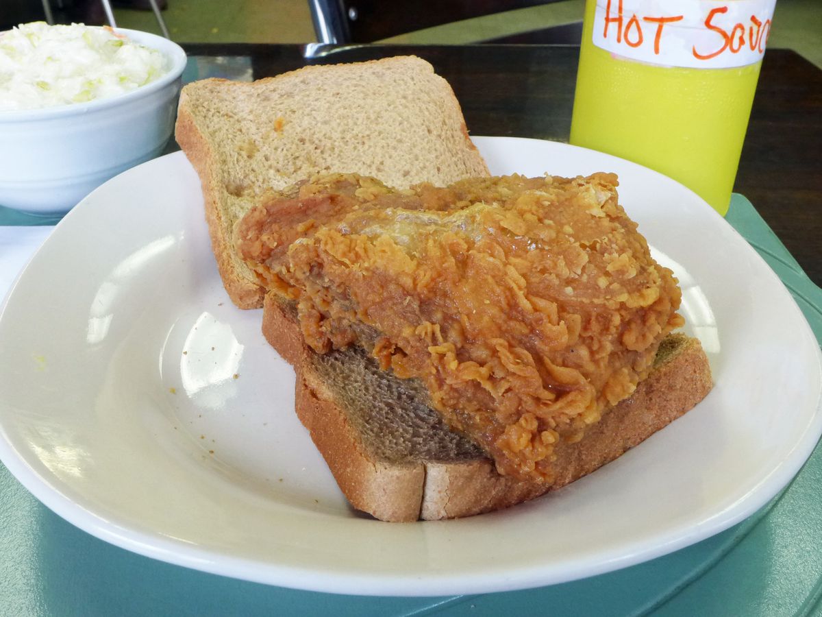 A fried chicken sandwich on whole wheat bread with a bottle of hot sauce in the background