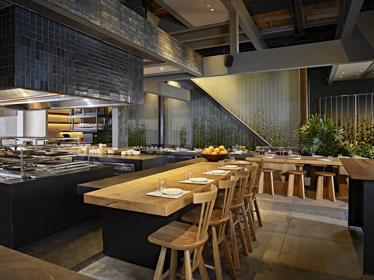 A wooden bar with seating faces the kitchen at Inko Nito, with slate gray walls and plants in the interior.