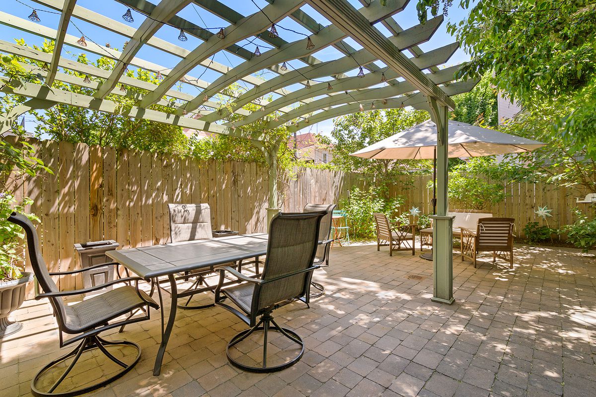 A backyard with tiles, wood fencing, two seating areas, and a green pergola.