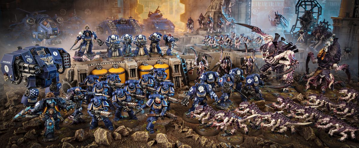 The full complement of miniatures in the Warhammer 40K: Leviathan boxed set in the foreground, and unrelated terrain and additional units in the background. Ultramarines, including many large Terminator Units and a mech, stand against a purple and bone group of Tyrranids, claws outstretched in fury.