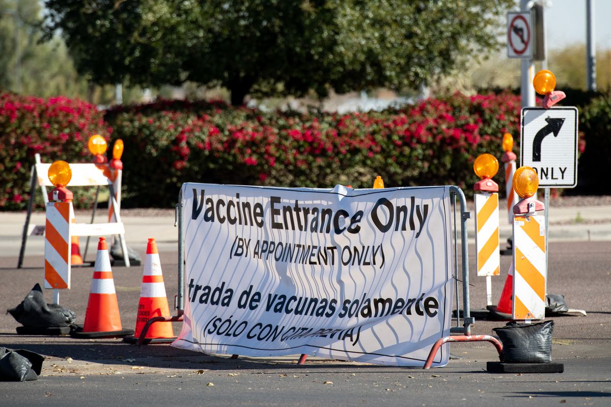 A sign on a street barricade reads “Vaccine entrance only, by appointment only” in English and in Spanish.