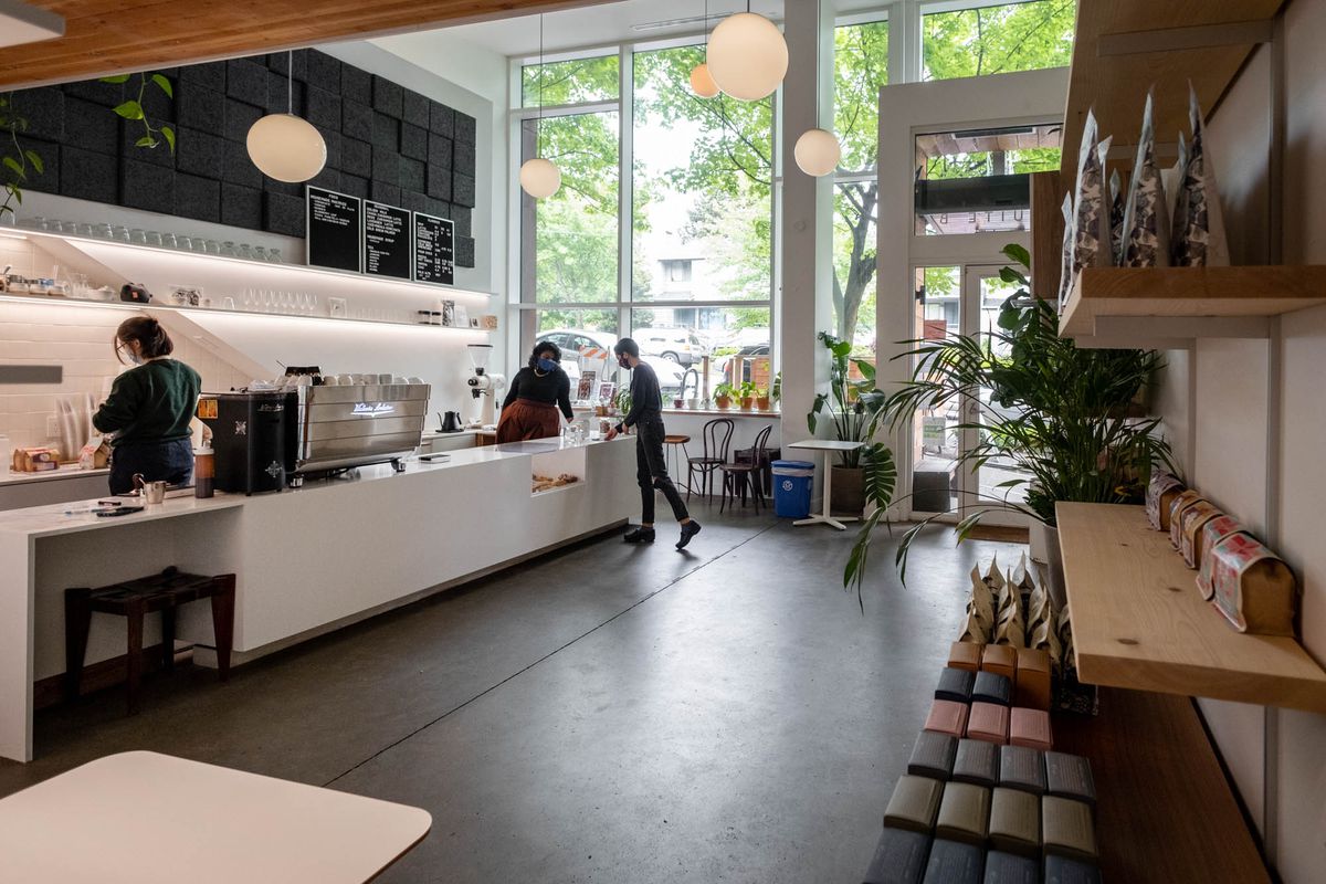 The inside of Union Coffee, looking out onto the street, with owner Geetu Vailoor speaking with a customer, and barista Grace Rathbone preparing a beverage