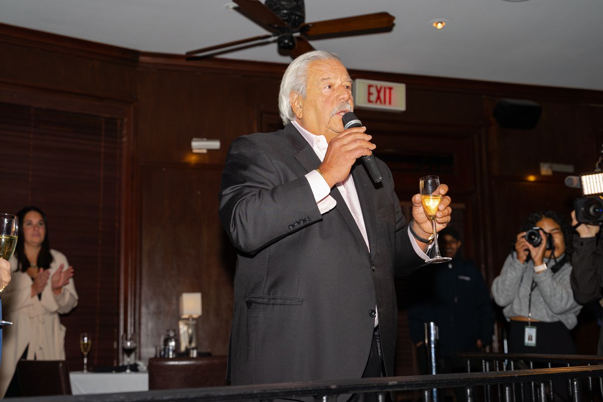 A man in a suit holding a microphone and a Champagne flute.