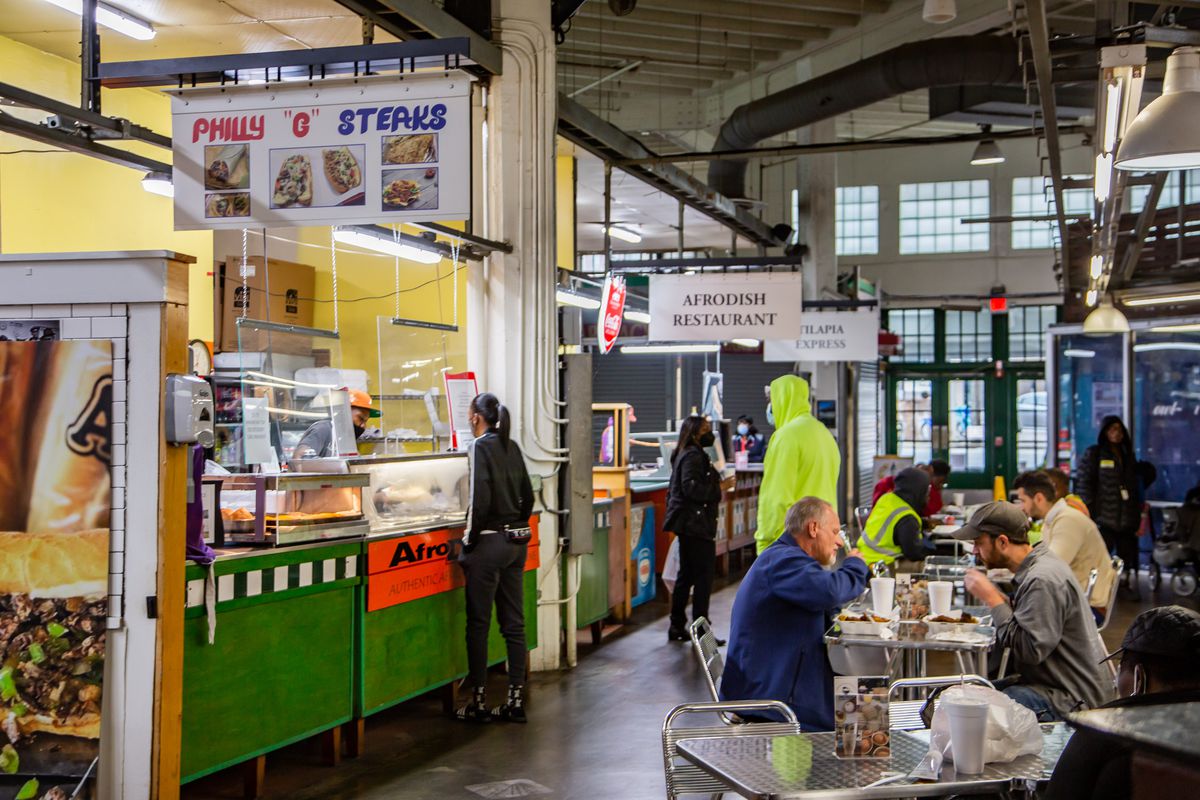 People order food from Philly G Steaks and AfroDish Restaurant stalls during lunch inside The Municipal Market of Atlanta, the Sweet Auburn Curb Market, as people sit at tables beyond eating. 