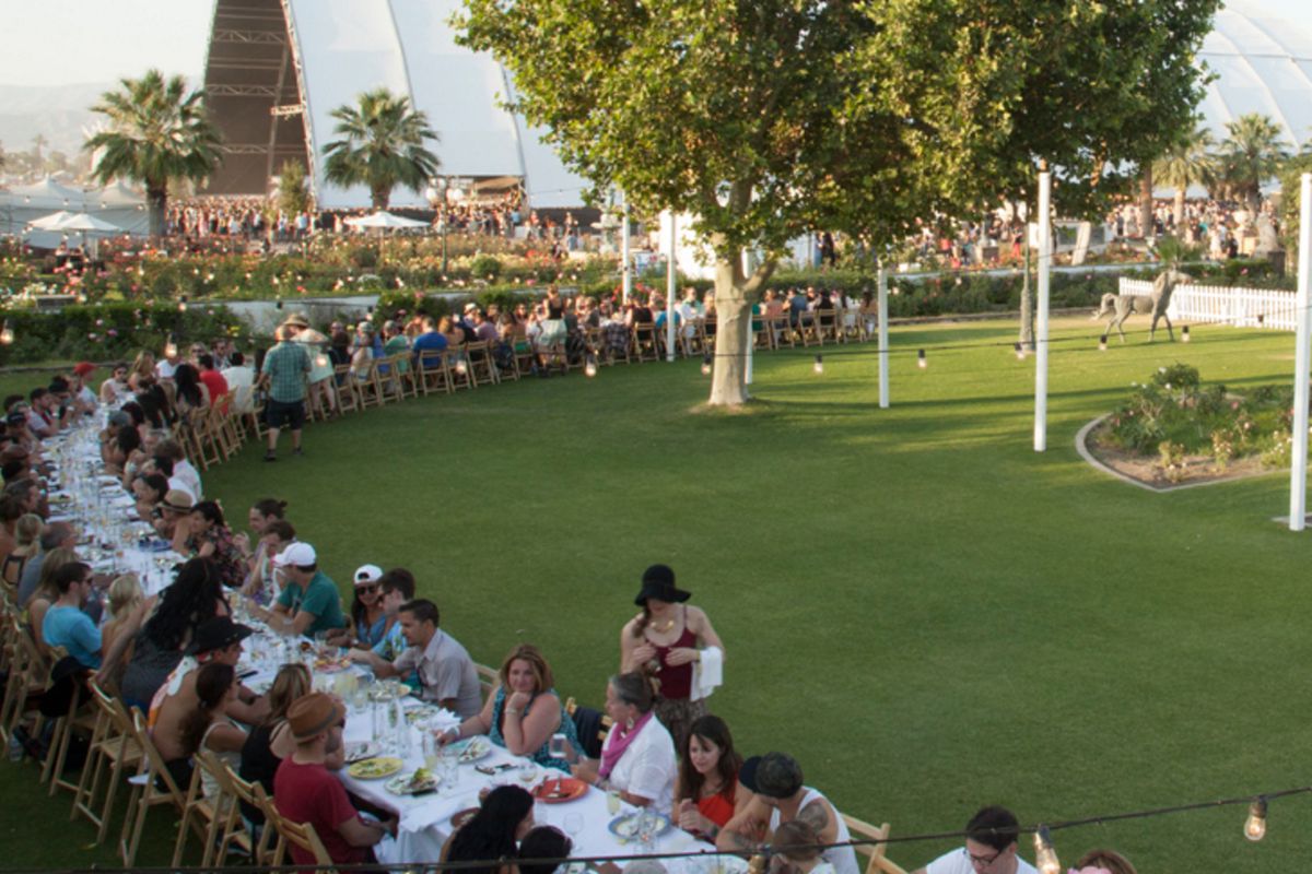 A long tableclothed-table full of diners in an outdoor field